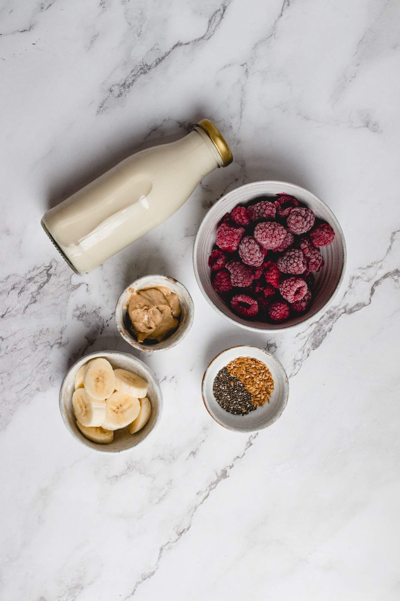 Ingredients for a raspberry smoothie including chia seeds, frozen raspberries, banana, almond milk, almond butter, and flax seeds.