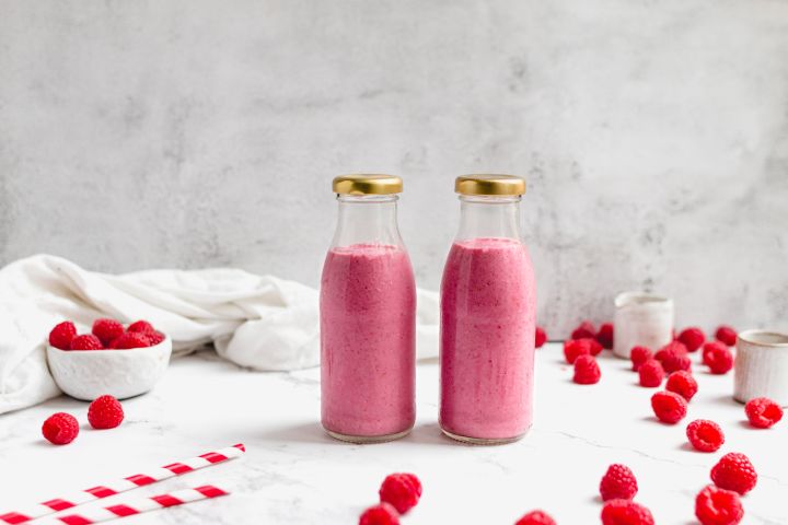 Raspberry chia smoothie with raspberries, chia seeds, almond butter, and almond milk in two glass bottles.