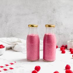 Raspberry chia smoothie with raspberries, chia seeds, almond butter, and almond milk in two glass bottles.