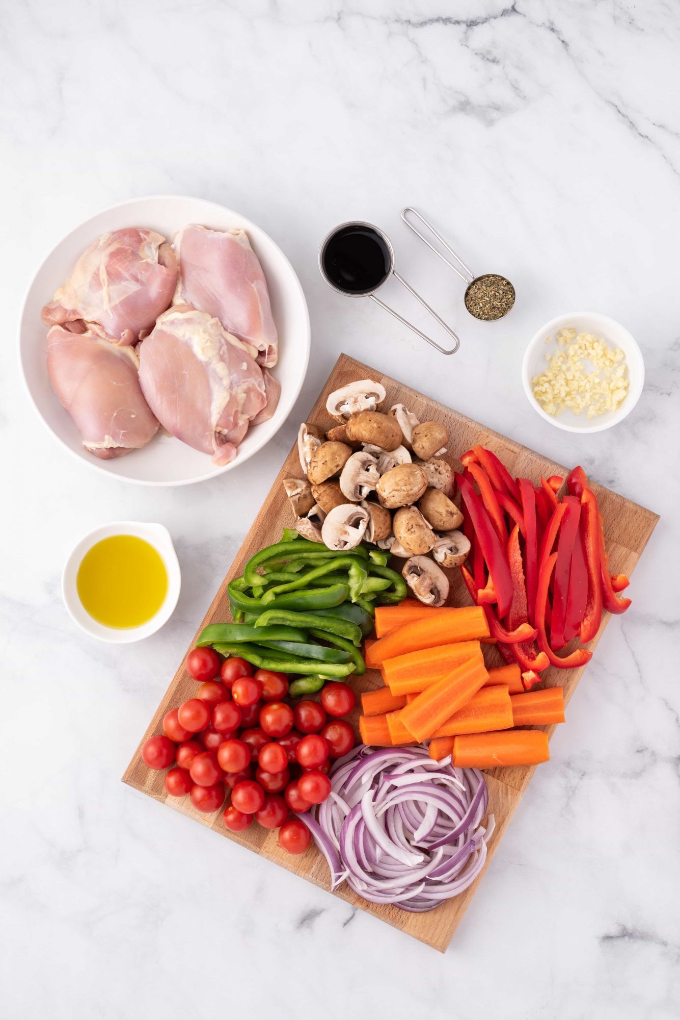 Ingredients for roasted balsamic chicken thighs and vegetables including mushrooms, peppers, carrots, tomatoes, onions, and balsamic vinegar.