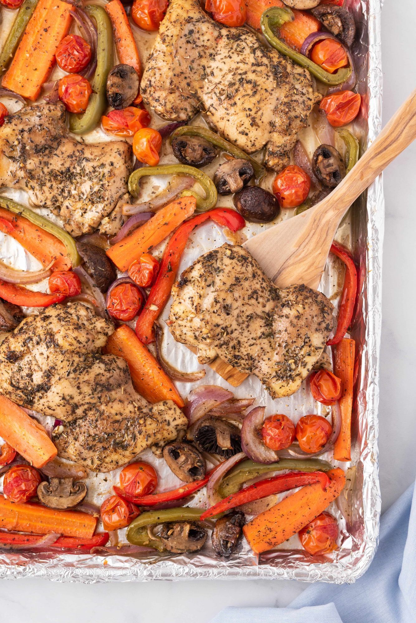 Sheet pan roasted chicken thighs with vegetables on a sheet pan with a wooden spatula. 