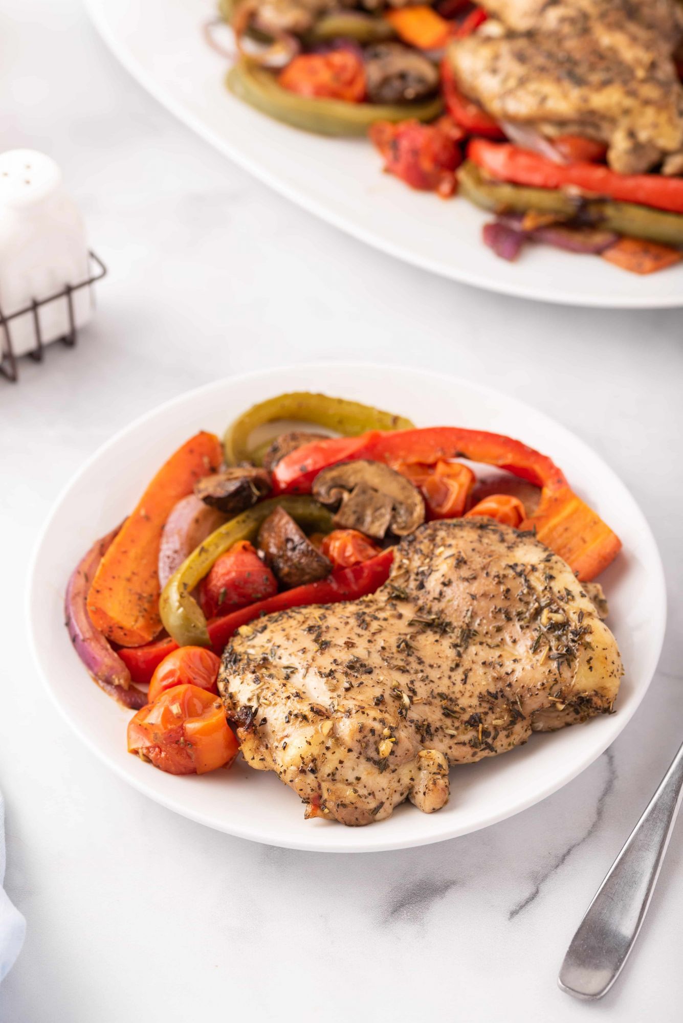 Balsamic vegetables and chicken thighs with tomatoes, carrots, peppers, and onions on a white plate.