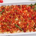 Roasted grape tomatoes on a baking sheet with olive oil, rosemary, salt, and pepper.