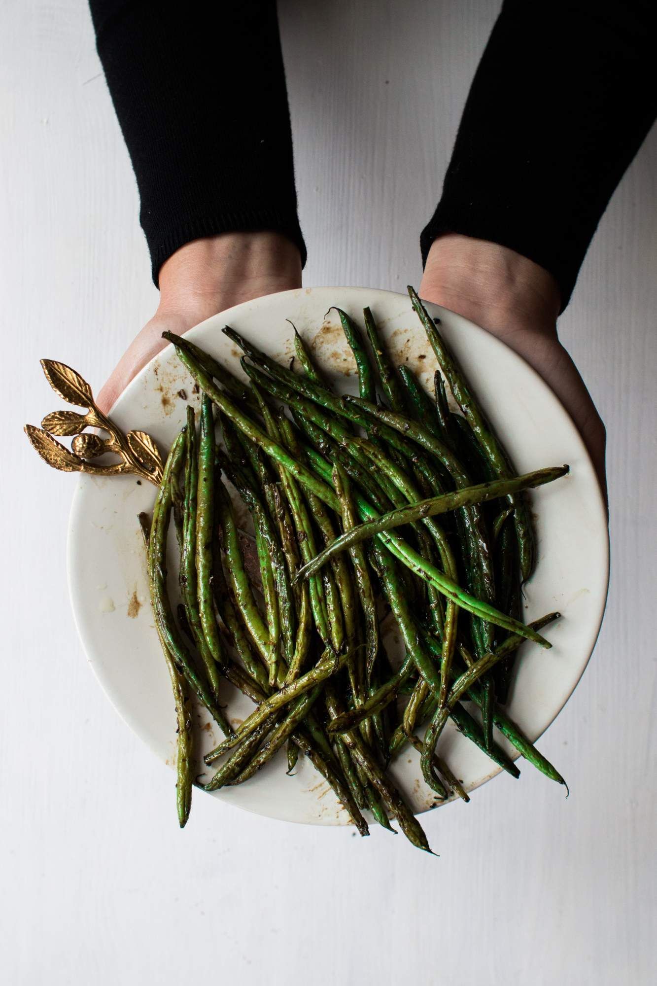 Roasted green beans on a wooden plate with garlic, salt, pepper, and olive oil. 