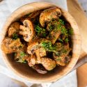 Roasted mushrooms with garlic, olive oil, and balsamic vinegar in a wooden bowl with fresh herbs. 