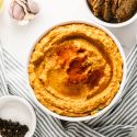 Roasted red pepper dip in a bowl drizzled with olive oil with garlic, crackers, and red bell pepeprs on the side.