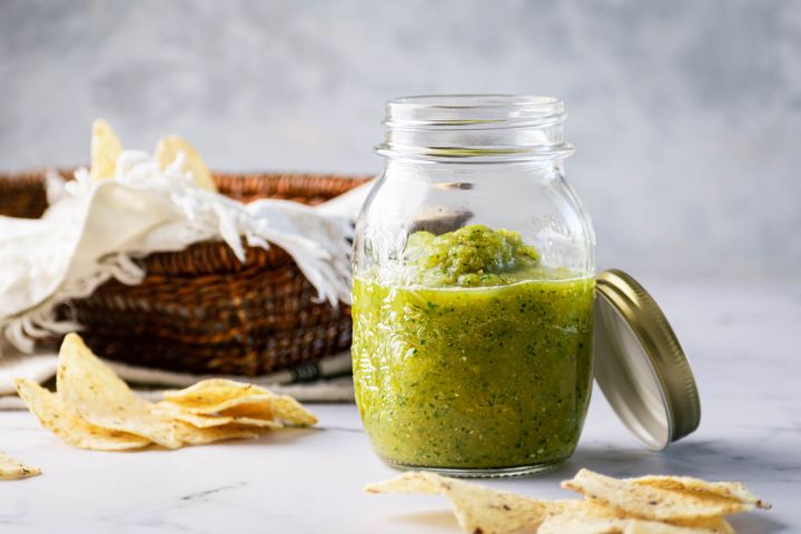 Roasted salsa verde with tomatillos, jalapenos, and cilantro in a mason jar with chips on the side.