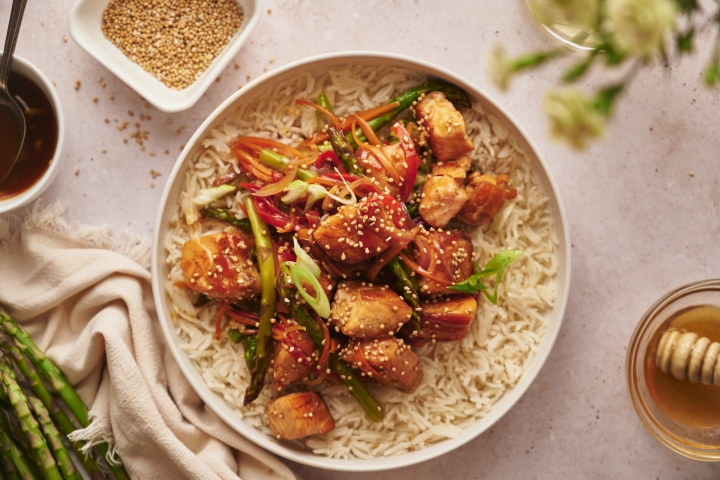 Salmon stir fry with chunks of salmon, asparagus, carrots, and red pepper in a bowl with steamed rice. 