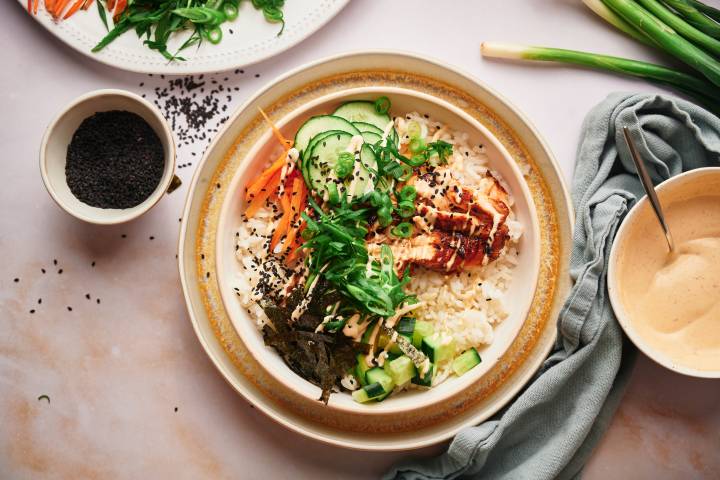 Salmon sushi bowls with sushi rice, salmon, seaweed strips, carrots, cucumbers, and spicy mayo. 