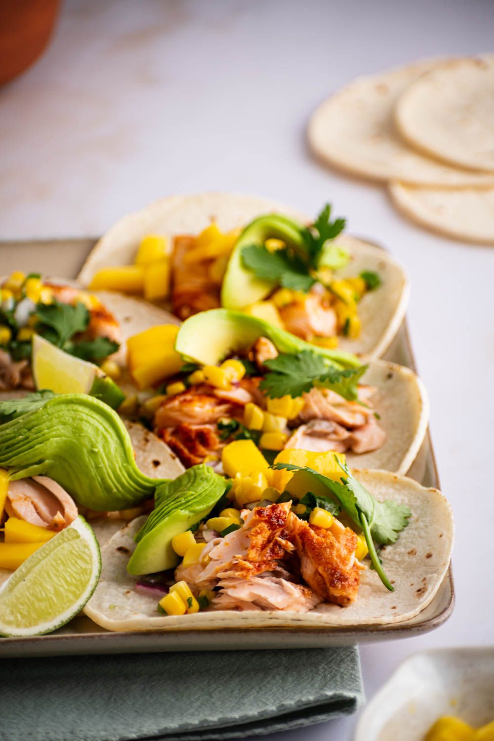 Baked salmon tacos with corn salsa, mango, avocado, and limes in flour tortillas.