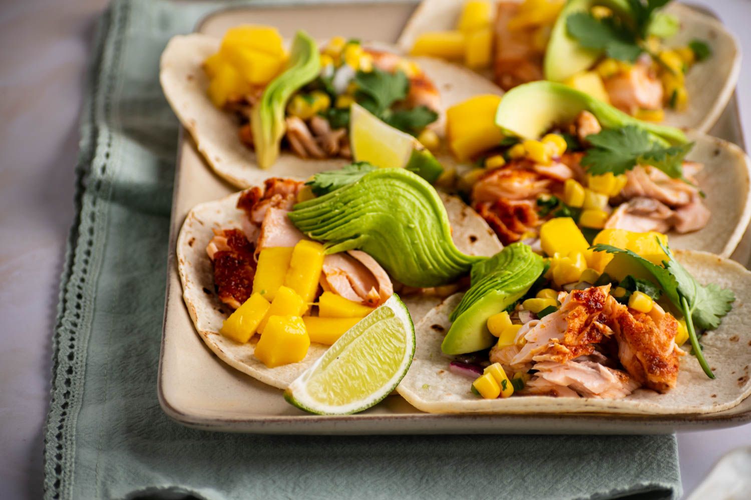 Spice rubbed salmon tacos in a tray with flour tortillas, limes, avocado, corn salsa, and mango.