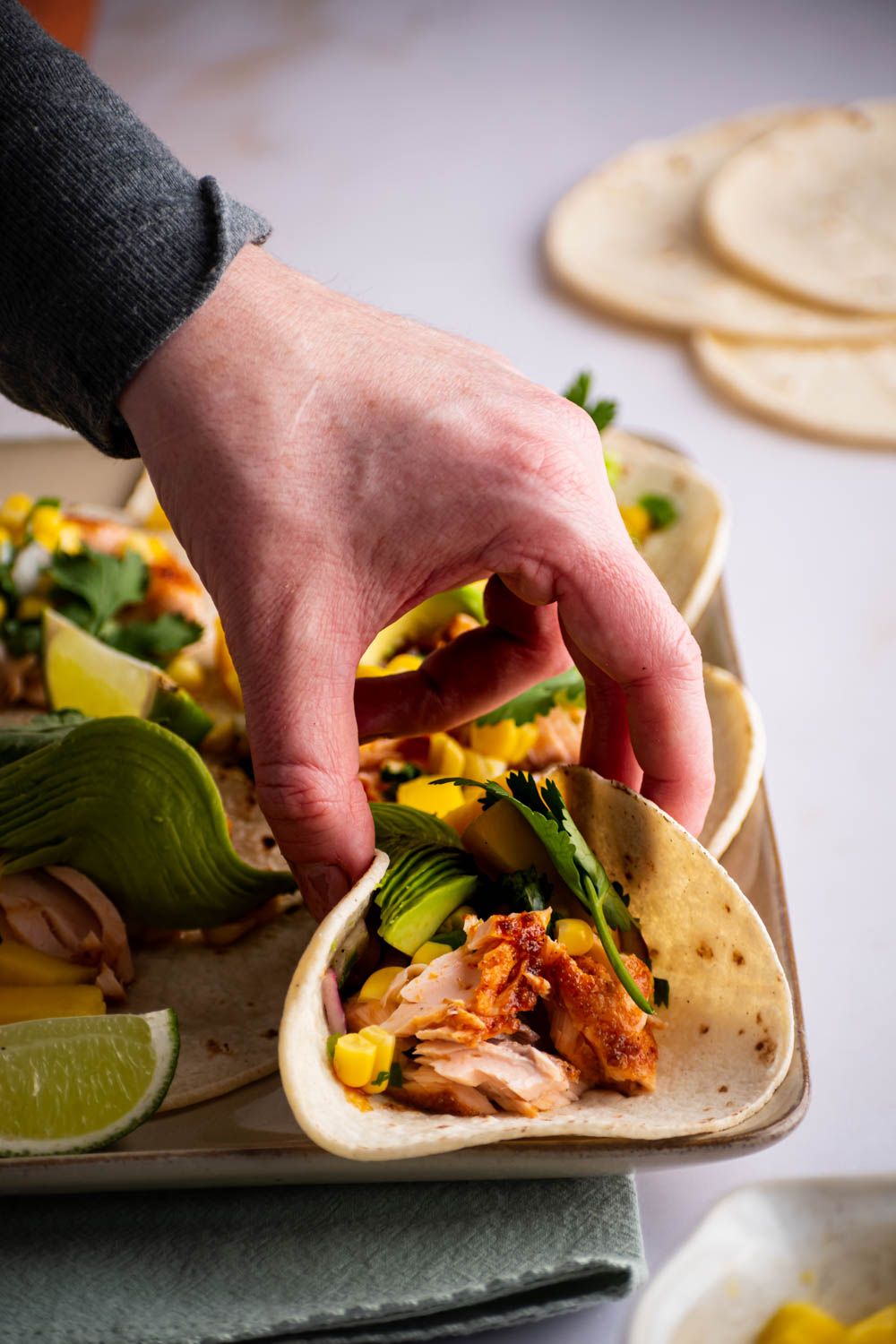 Hand picking up a blackened salmon taco with avocado and corn salsa.