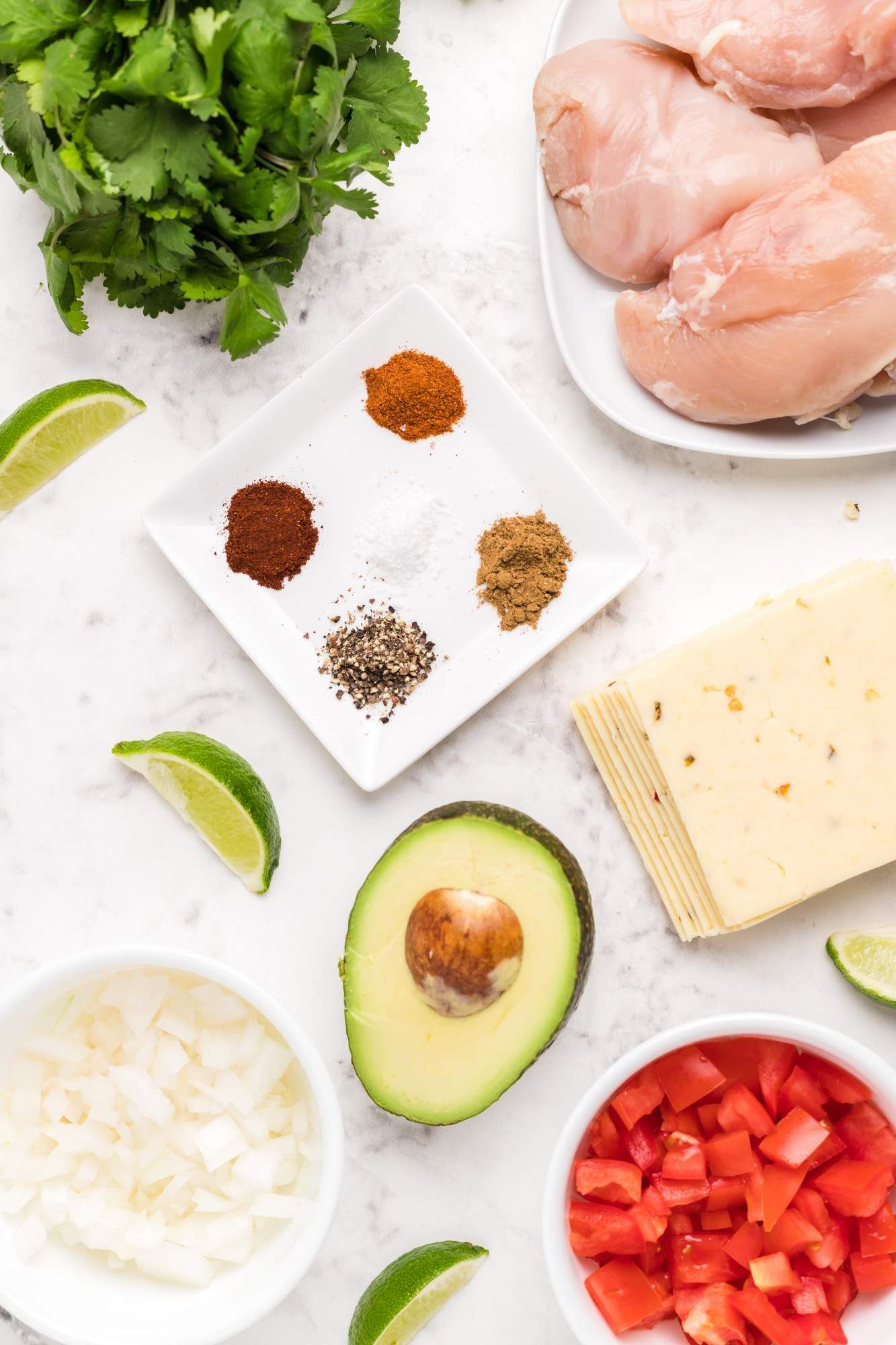 Ingredients for baked salsa chicken including chicken breasts, pico de gallo, cilantro, cheese, and limes.