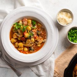 Slow cooker sausage and gnocchi soup with mushrooms, spinach, Parmesan cheese, and a rich tomato broth in a bowl.