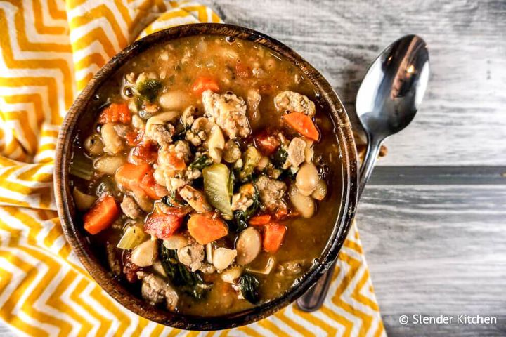 Sausage white bean soup with spinach, carrots, onions, and tomatoes in a wooden bowl.