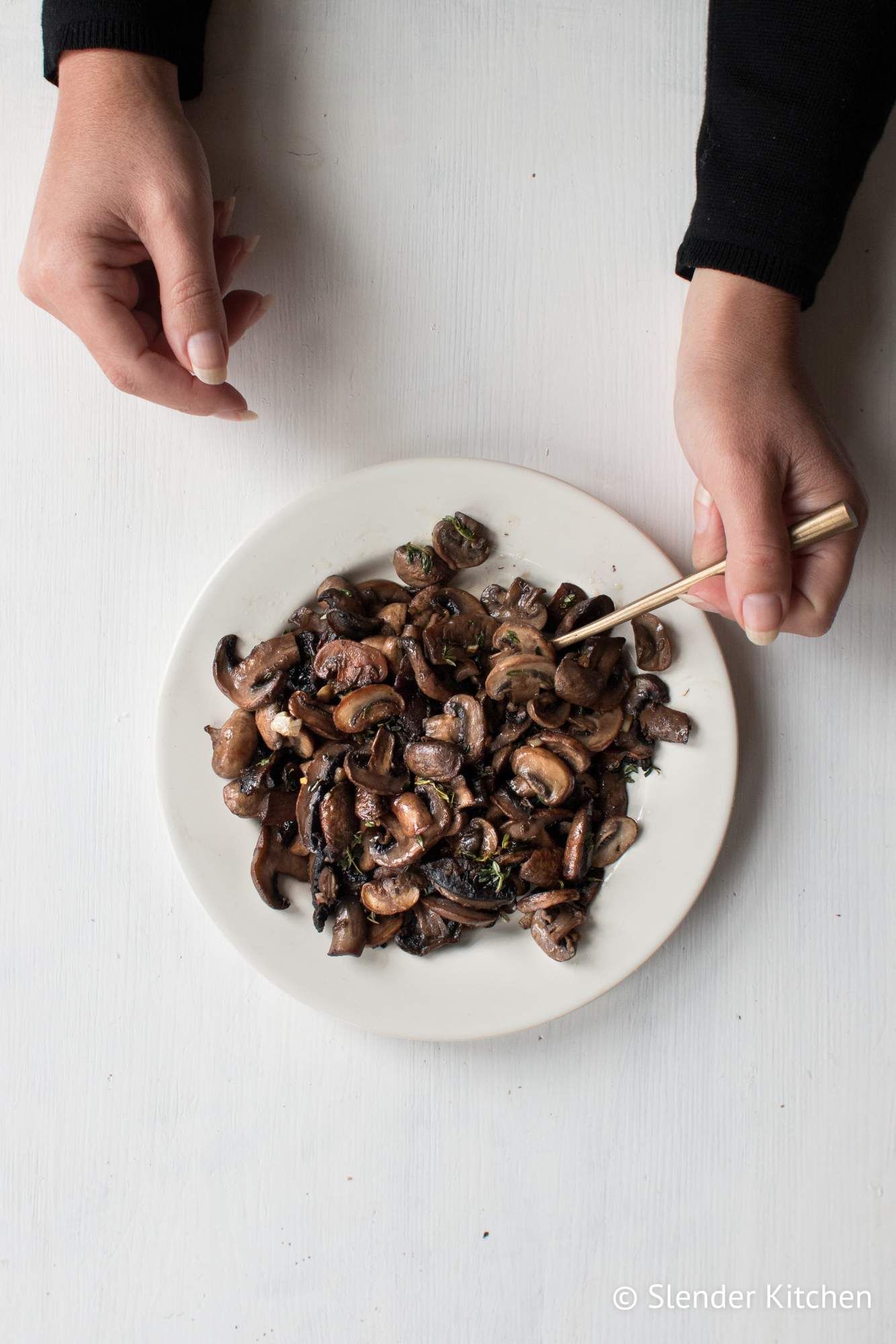 Garlic mushrooms that are sauteed and served on a plate with two hands on the side.