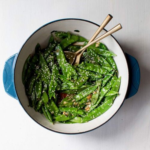 Sauteed snow peas with green onions, soy sauce, garlic, ginger, and sesame seeds with chopsticks.