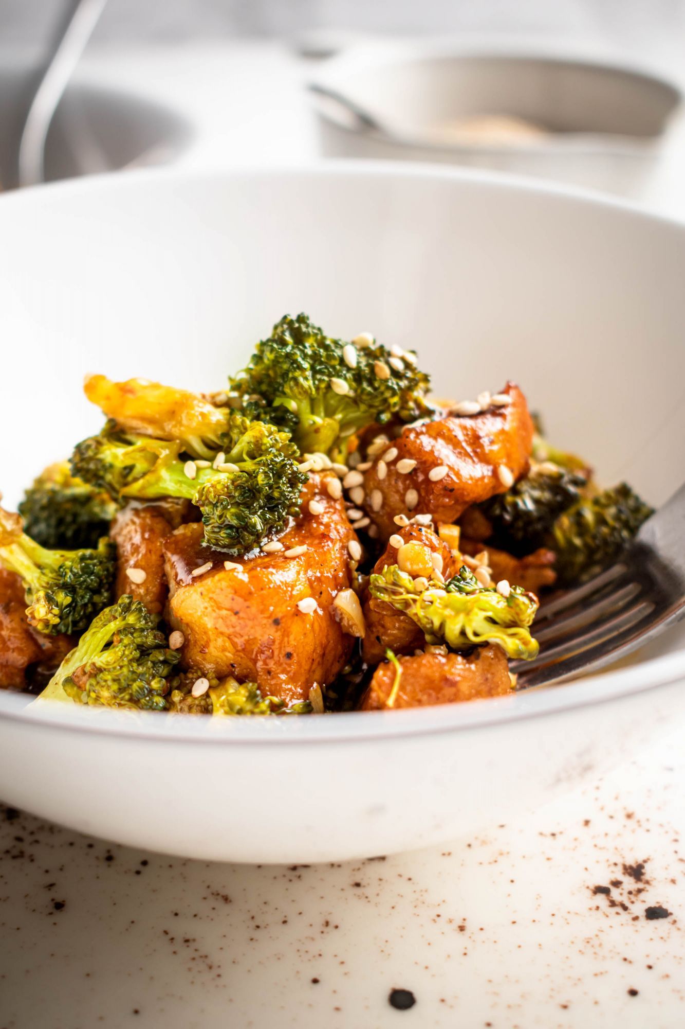 Chinese sesame chicken and broccoli served with sesame sauce and sesame seeds on the side.