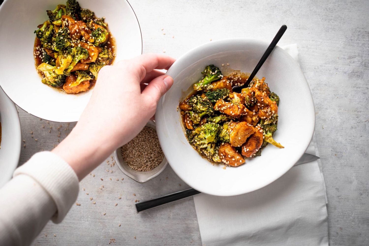 Two bowls of takeout inspired sesame chicken breast with broccoli florets sprinkled with sesame seeds.