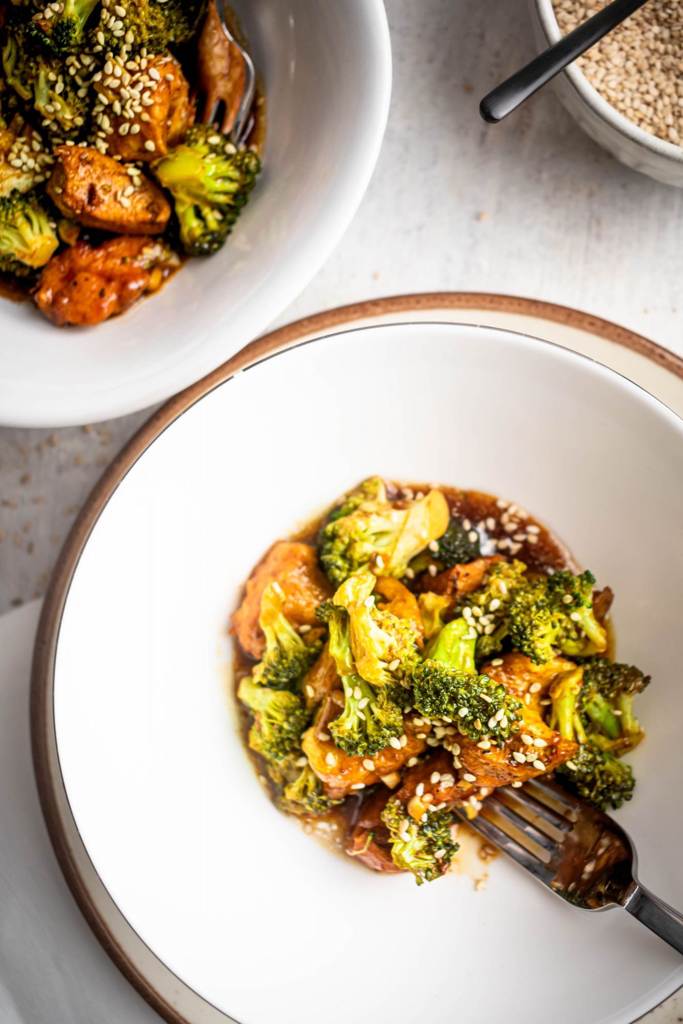 Healthier chicken and broccoli with sesame sauce and sesame seeds served in two bowls.