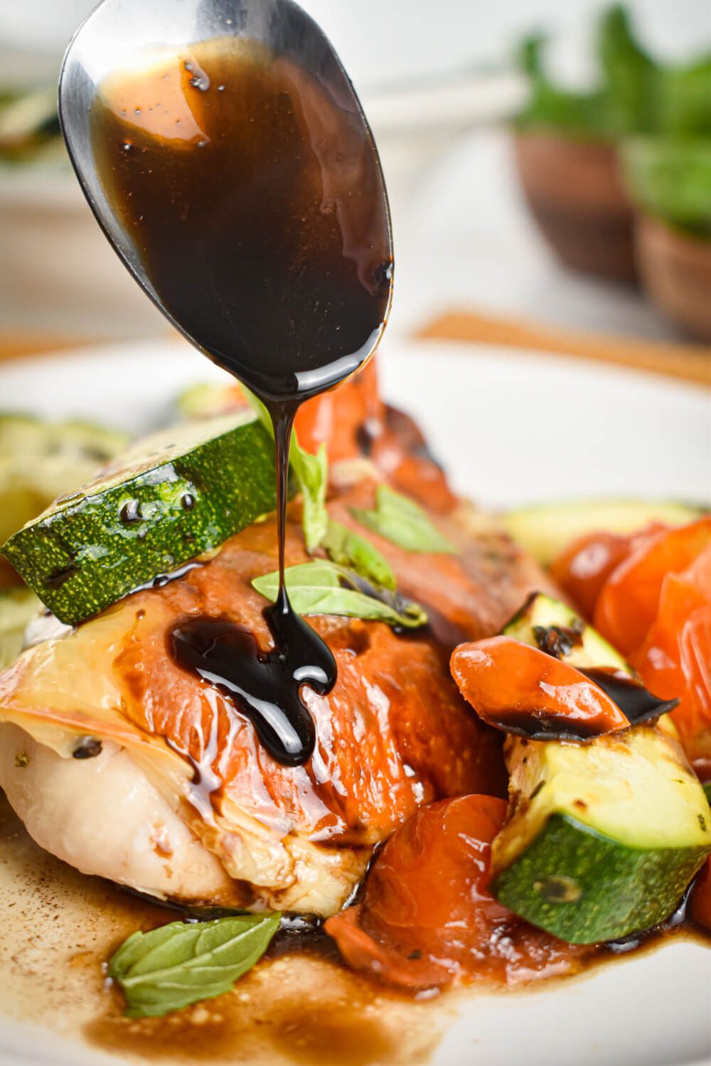 Chicken caprese with zucchini, tomatoes, basil, mozzarella cheese, and balsamic vinegar on a plate with a spoon.