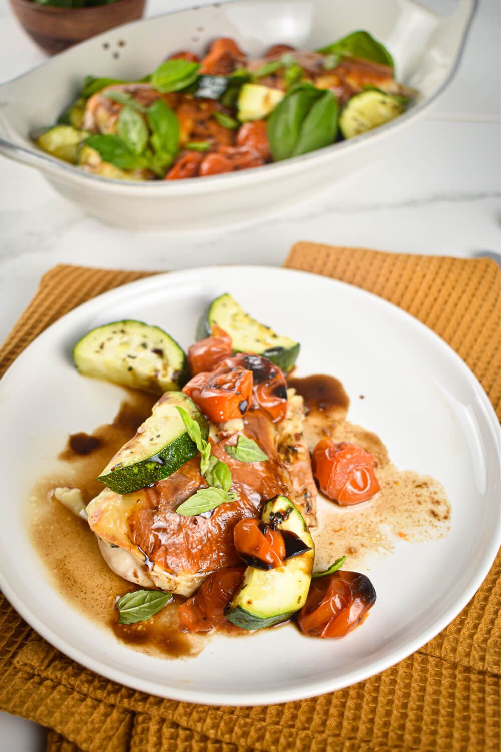 Sheet pan caprese chicken in a dish with melted cheese, tomatoes, zucchini, and balsamic vinegar.