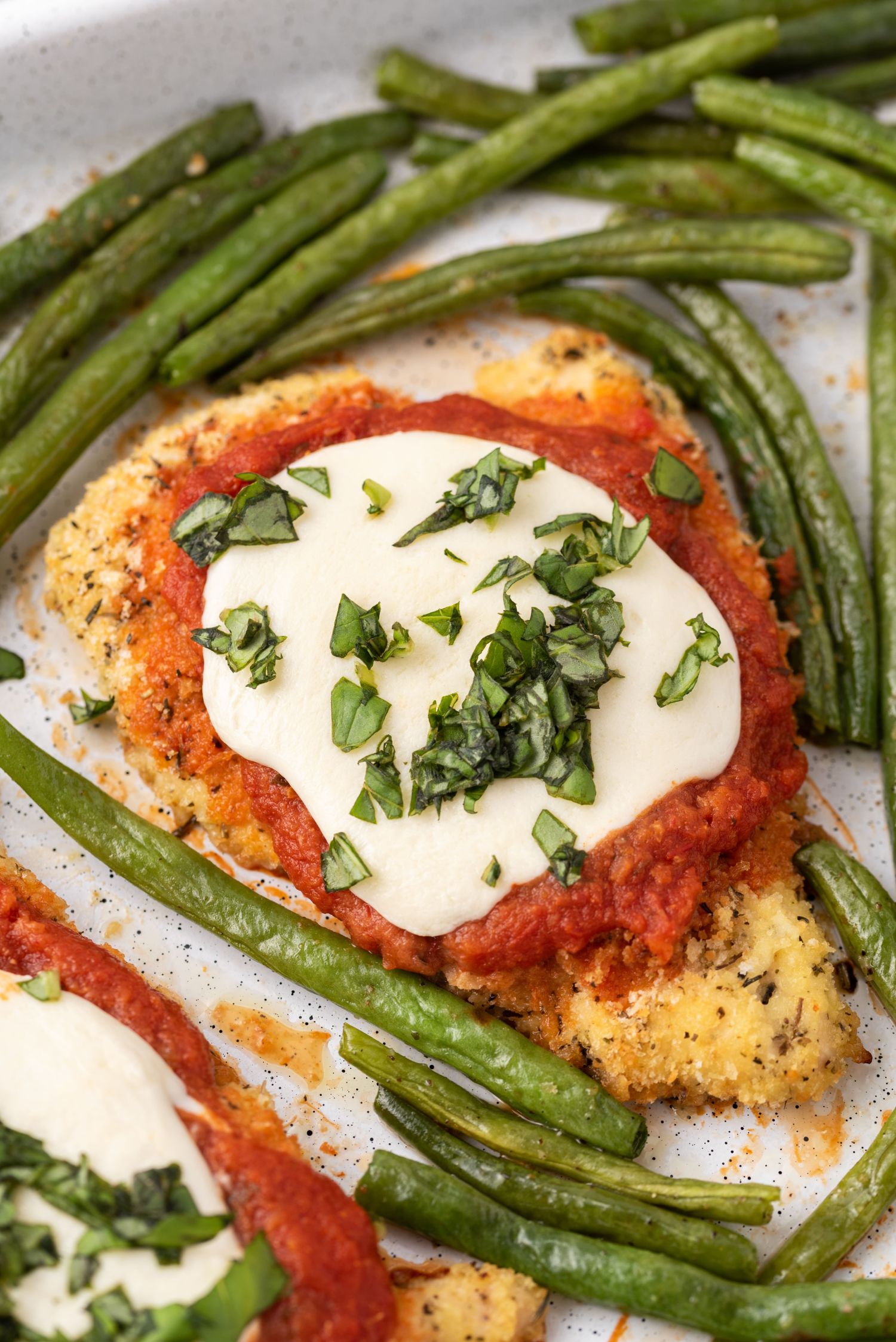 Sheet pan chicken parmesan with marinara sauce, melted fresh mozzarella, and green beans.