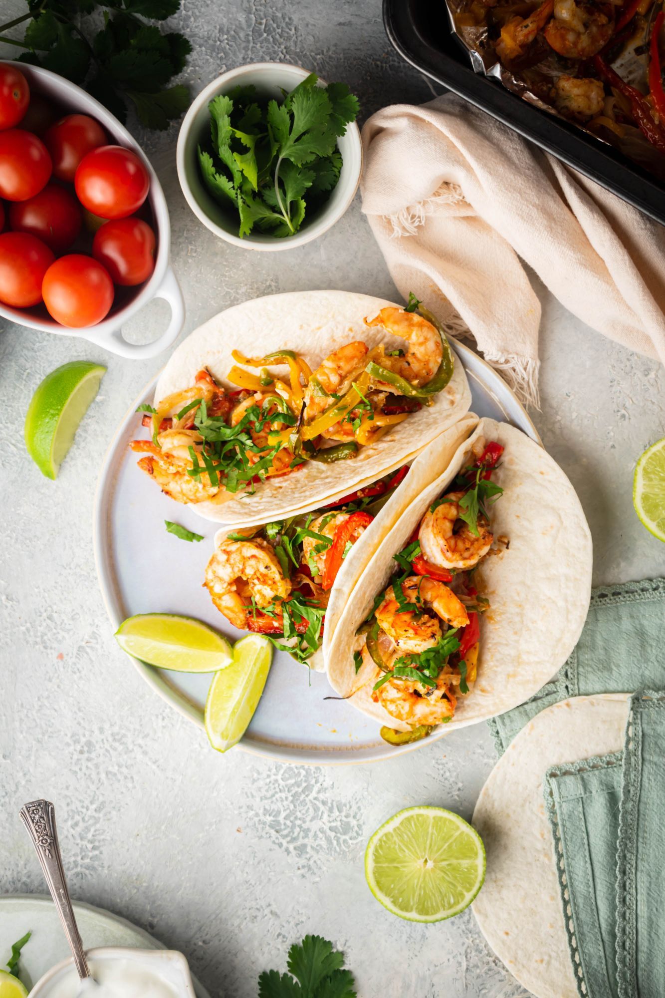 Shrimp fajitas with bell peppers, onions, and fajita seasoned shrimp served on flour tortillas with lime wedges and cilantro.