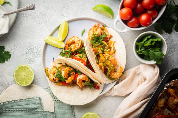 Sheet pan shrimp fajitas with peppers and onions served on flour tortillas with lime and cilantro.