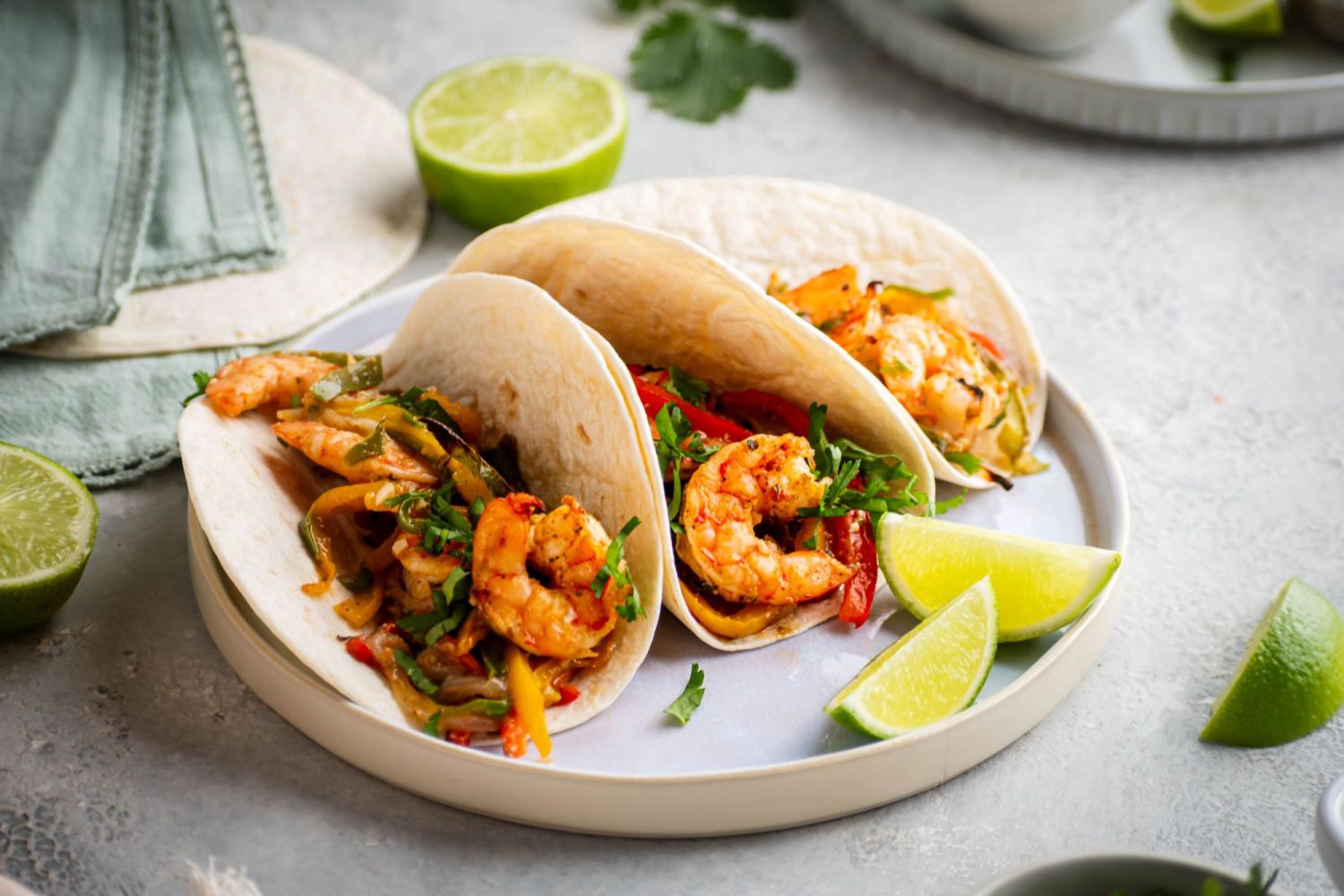 Fajitas with shrimp, peppers, and onions served with tortillas, cilantro, sour cream, tomatoes, and limes. 