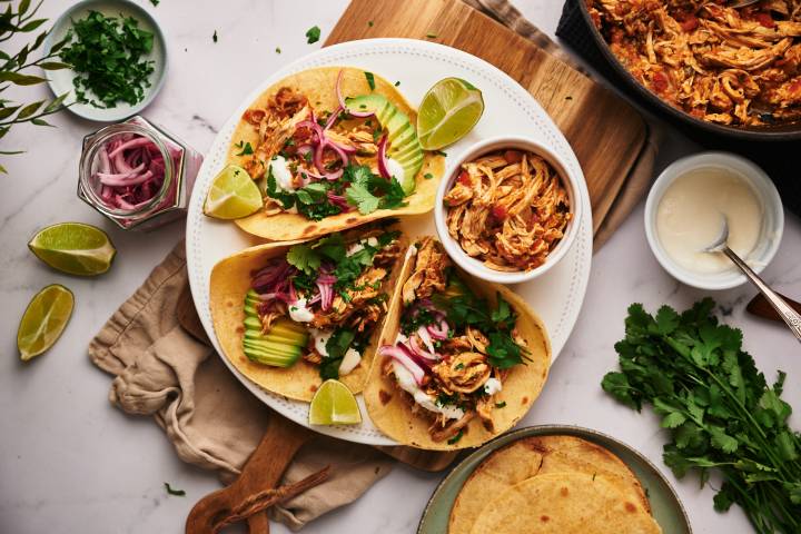 Shredded chicken tacos with avocado, pickled onions, cilantro, and limes on a plate.