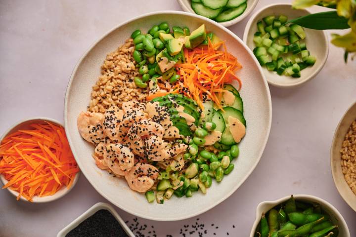 Sushi bowls with spicy shrimp, avocado, cucumbers, carrots, and edamame with brown rice.