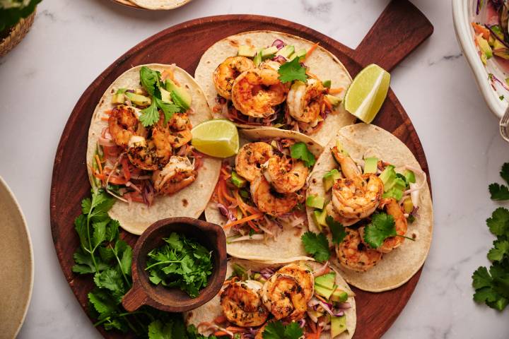 Shrimp tacos with slaw served on corn tortillas with avocado, lime, and fresh cilantro.