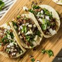 Slow cooker beef barbacoa tacos on corn tortillas with onion, cilantro, and queso fresco.