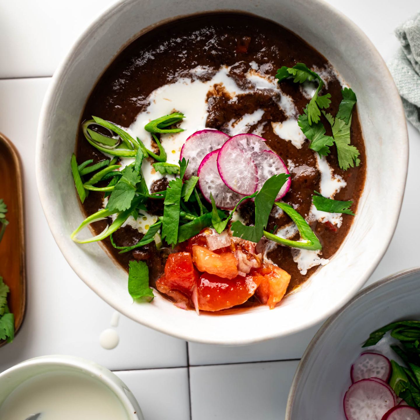 Slow cooker Black Bean Soup in a bowl with sour cream, cilantro, tomatoes, and radishes.