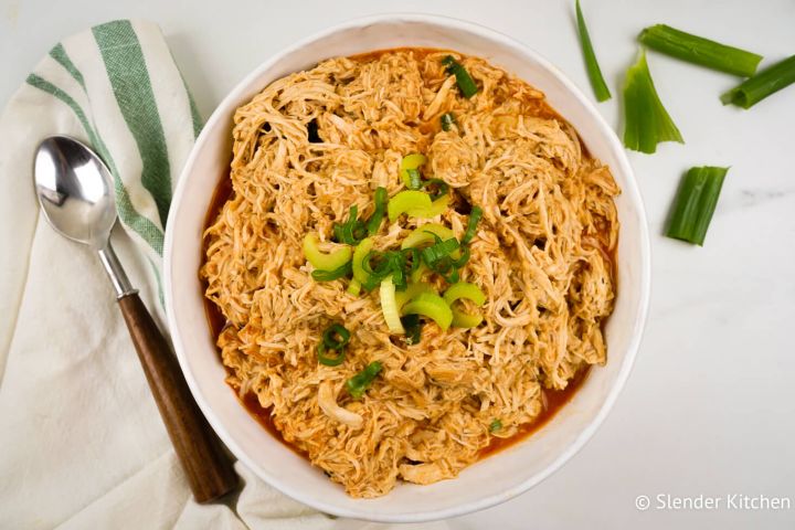 Slow cooker buffalo chicken shredded in a bowl with diced celery and buffalo sauce.