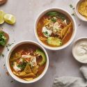 Slow Cooker Chicken Fajita Soup in tow bowls with shredded chicken, bell peppers, onions tortilla chips, and avocado.