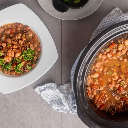 Crockpot charro beans in a bowl with Mexican pinto beans, onions, jalapenos, and spices with a slow cooker on the side.