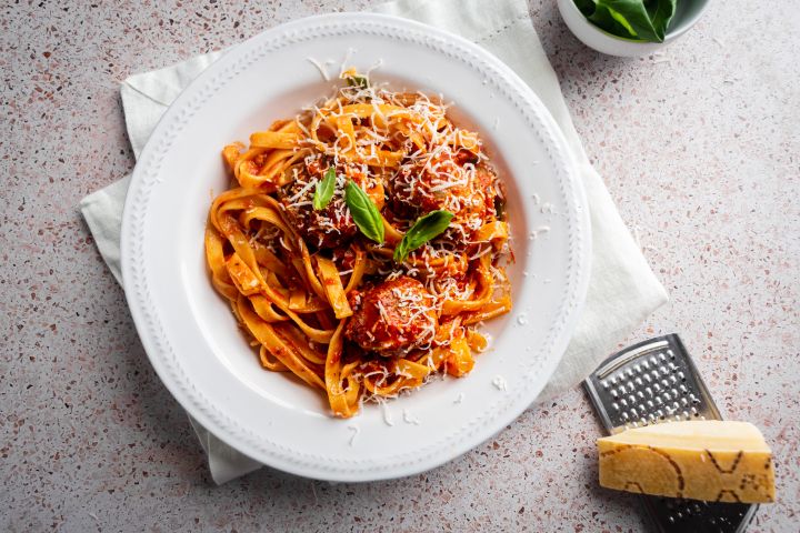 Slow cooker Italian meatballs served with pasta, parmesan cheese, and fresh basil.