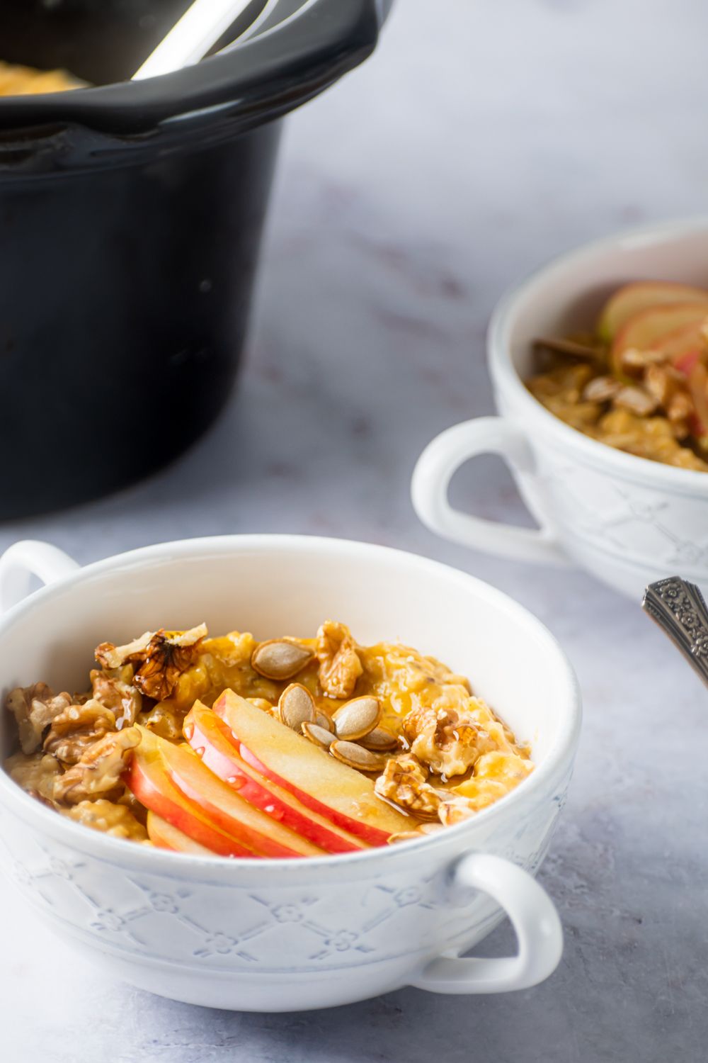 Steel cut oatmeal with canned pumpkin, pumpkin pie spices, chia seeds, and flax in a mug with apples and pumpkin seeds.