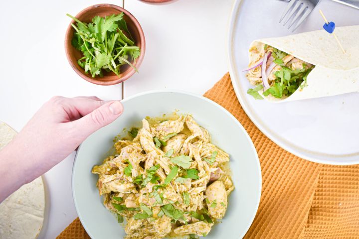 Slow cooker salsa verde chicken in a bowl with shredded chicken, green salsa, and fresh cilantro.