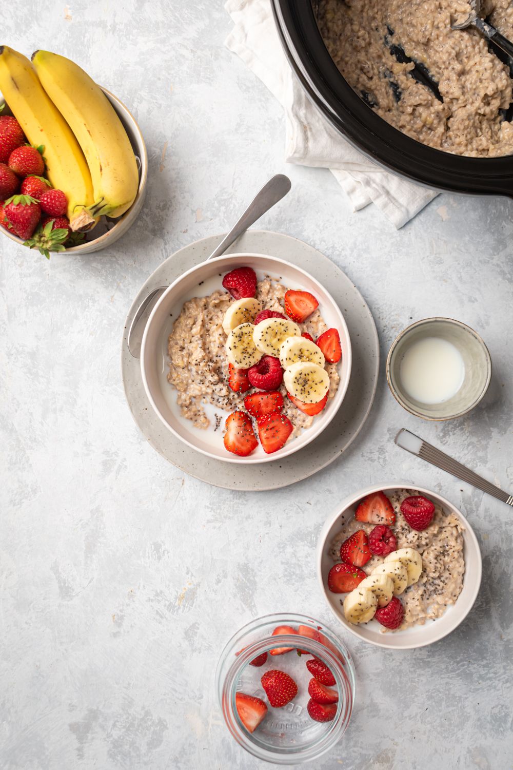 Crockpot steel cut oatmeal served in two bowls with fresh fruit and a slow cooker with oats on the side.