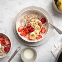 Slow cooker steel cut oatmeal in two bowls with bananas, raspeberries, strawberries, and milk.