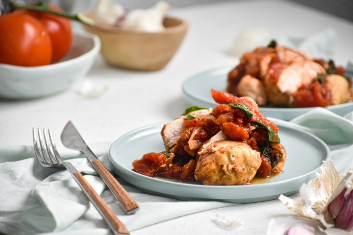 Slow cooker tomato balsamic chicken sliced and served with spinach and basil on a plate.