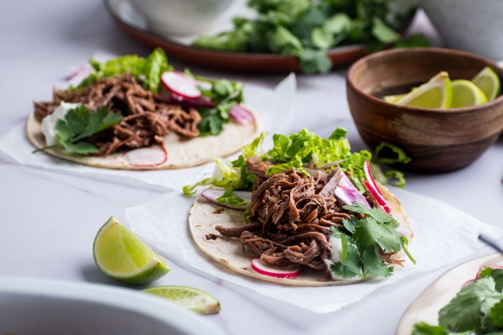 Slow cooker tri tip tacos on white corn tortillas with lettuce, cilantro, and radishes.