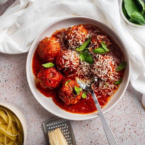 Slow cooker turkey meatballs in a shallow bowl with marinara sauce, fresh basil, and Parmesan cheese. 