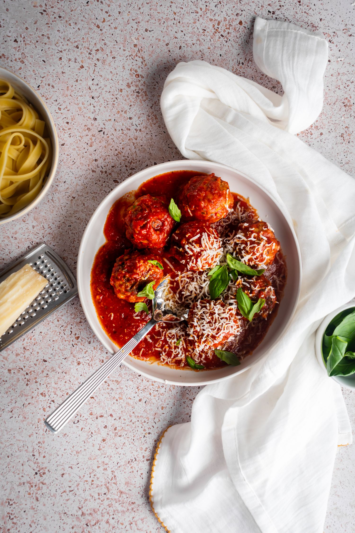 Bowl of turkey meatballs with spaghetti sauce served with pasta and Parmesan cheese on the side.