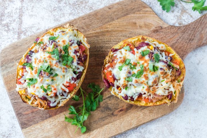 Spaghetti squash burrito bowls with beans, peppers, onions, seasoning, and melted cheese on a cutting board.