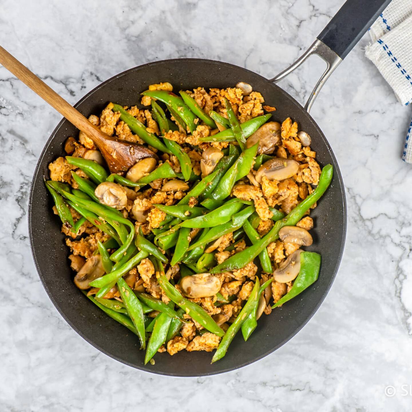 Spicy Ground Turkey stir fry with green beans and mushrooms in a black skillet with a wooden spoon.