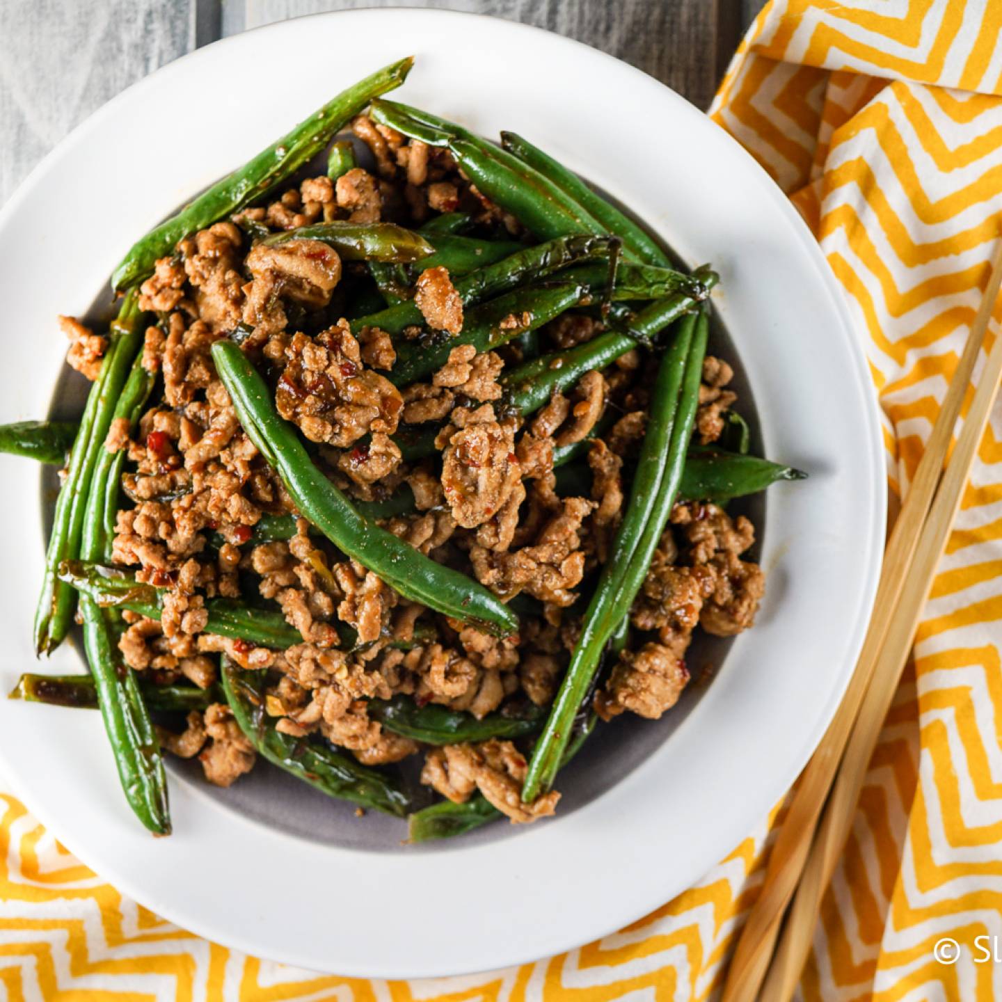 Ground turkey and green bean stir fry in a bowl with spicy sauce and chopsticks.